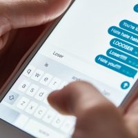 partial view of abuser sending offensive messages while using smartphone, illustrative editorial