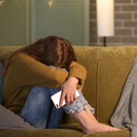 Offended teenage girl with mobile phone on sofa at night